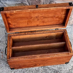 Könnte beinhalten: Eine Holzkiste mit einem Scharnierdeckel und drei Fächern im Inneren. Die Kiste ist aus Naturholz mit brauner Beize und schwarzen Metallverzierungen.