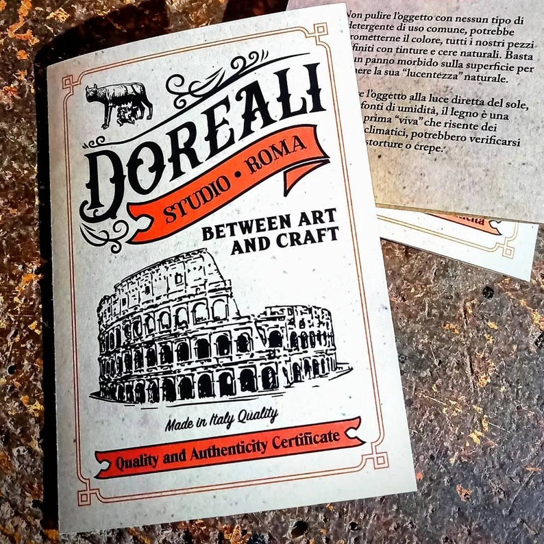 May include: A cream-colored card with the text "DOREALI STUDIO ROMA BETWEEN ART AND CRAFT" and an illustration of the Colosseum. The card also includes the text "Made in Italy Quality" and "Quality and Authenticity Certificate".