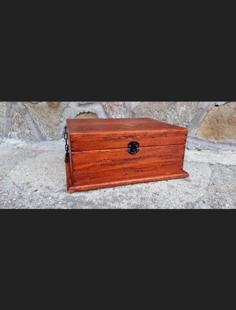 May include: A wooden box with a hinged lid and a metal latch. The box is stained a dark reddish-brown colour and has a chain attached to the lid.