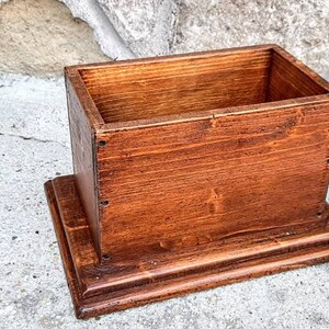 May include: A wooden box with a lid, stained a rich brown color. The box is sitting on a raised base, also made of wood.