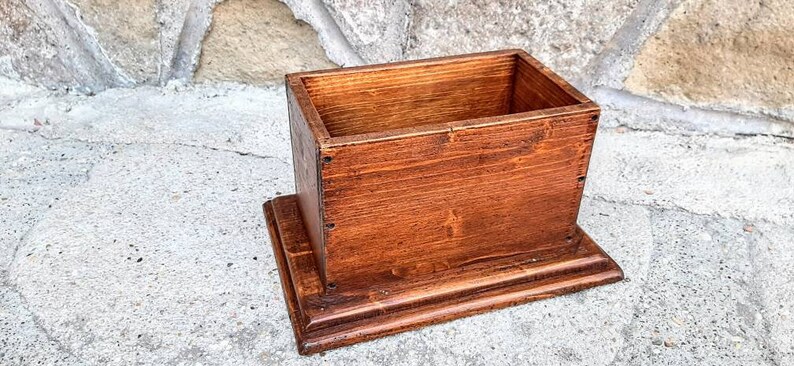 May include: A wooden box with a lid, stained a rich brown color. The box is sitting on a raised base, also made of wood.