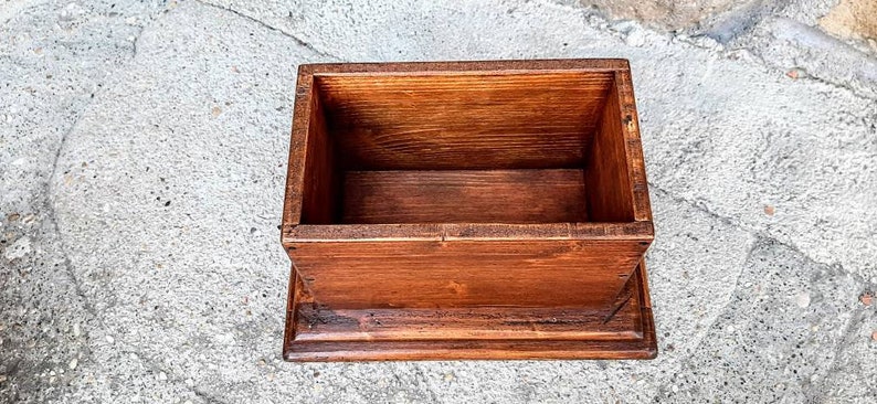 May include: A wooden box with a hinged lid and a base. The box is made of natural wood with a rich brown stain. The box is empty and ready to be filled.