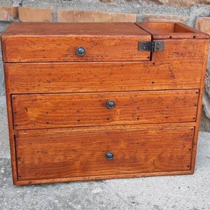May include: A wooden box with four drawers and a hinged top. The box is stained a dark brown color and has metal handles on each drawer.