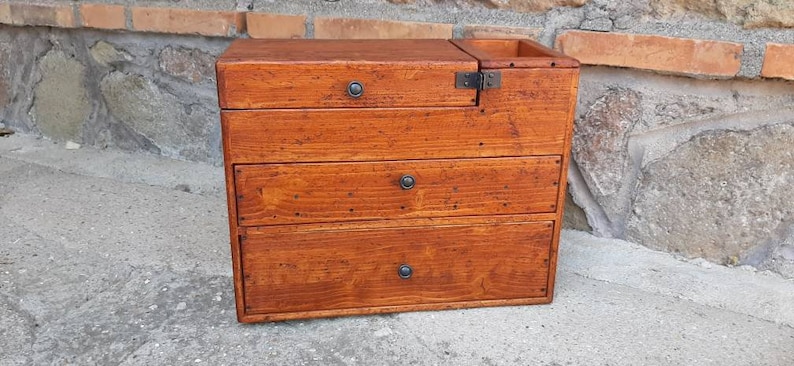 May include: A wooden box with four drawers and a hinged top. The box is stained a dark brown color and has metal handles on each drawer.