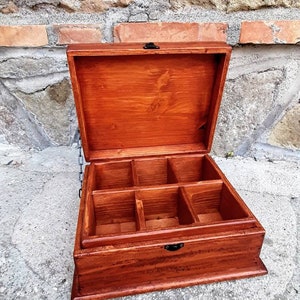 May include: A wooden box with a hinged lid and multiple compartments. The box is stained a rich reddish-brown colour and has black metal hinges.