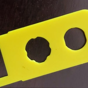 May include: A yellow plastic tool with two circular cutouts. The tool is designed to help open jars.
