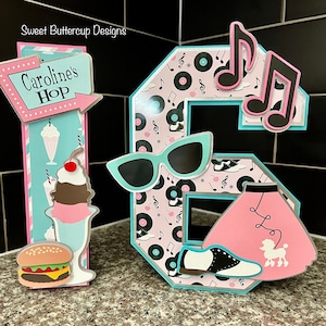 May include: A 3D number 16 decoration featuring a 1950s diner theme. The number 1 is a sign reading Caroline's Hop with a milkshake and burger. The number 6 features musical notes, vinyl records, cat-eye glasses, a poodle skirt, and saddle shoes.