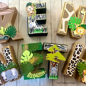 Puede incluir: Un conjunto de letras de madera decorativas que deletrean "WELCOME", cada una adornada con dise&ntilde;os tem&aacute;ticos de la jungla. Las letras presentan estampados de animales de safari, sombreros de safari y follaje de la jungla, con recortes de animales.