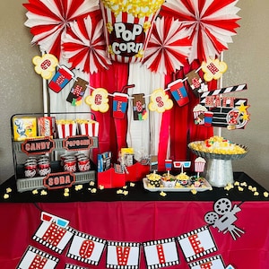 K&ouml;nnte beinhalten: Eine Filmabend-Partydekoration mit einem Popcorn-Ballon, rot-wei&szlig;en Papierf&auml;chern und einem Banner mit der Aufschrift MOVIE NIGHT. Der Tisch enth&auml;lt ein mehrst&ouml;ckiges Metalltablett mit S&uuml;&szlig;igkeiten, Limonaden, Popcornbeh&auml;ltern und einem Filmklappen-Schild.