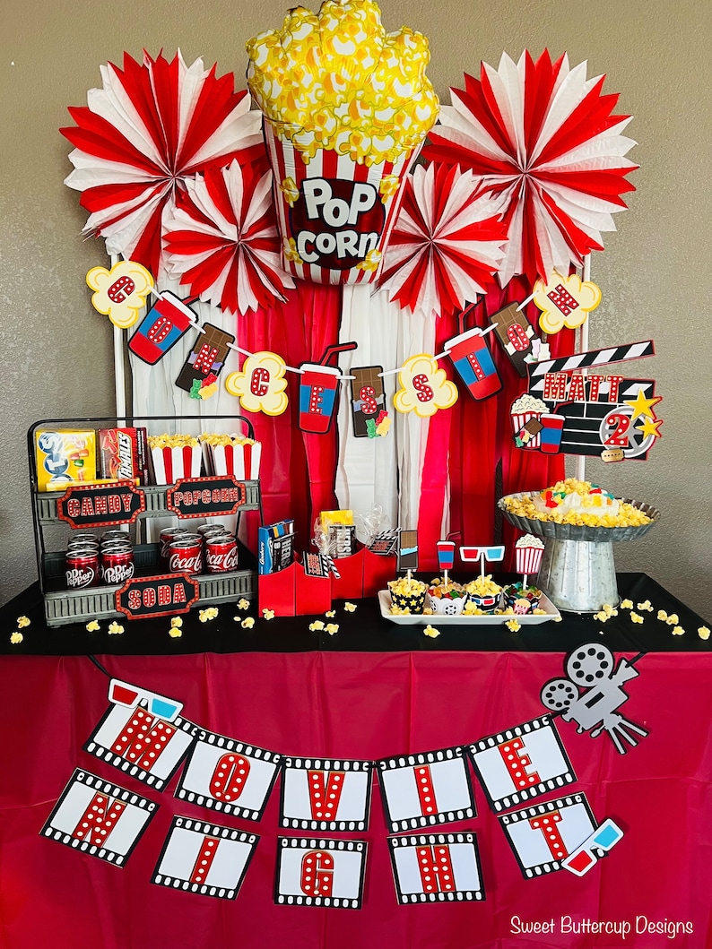 K&ouml;nnte beinhalten: Eine Filmabend-Partydekoration mit einem Popcorn-Ballon, rot-wei&szlig;en Papierf&auml;chern und einem Banner mit der Aufschrift MOVIE NIGHT. Der Tisch enth&auml;lt ein mehrst&ouml;ckiges Metalltablett mit S&uuml;&szlig;igkeiten, Limonaden, Popcornbeh&auml;ltern und einem Filmklappen-Schild.