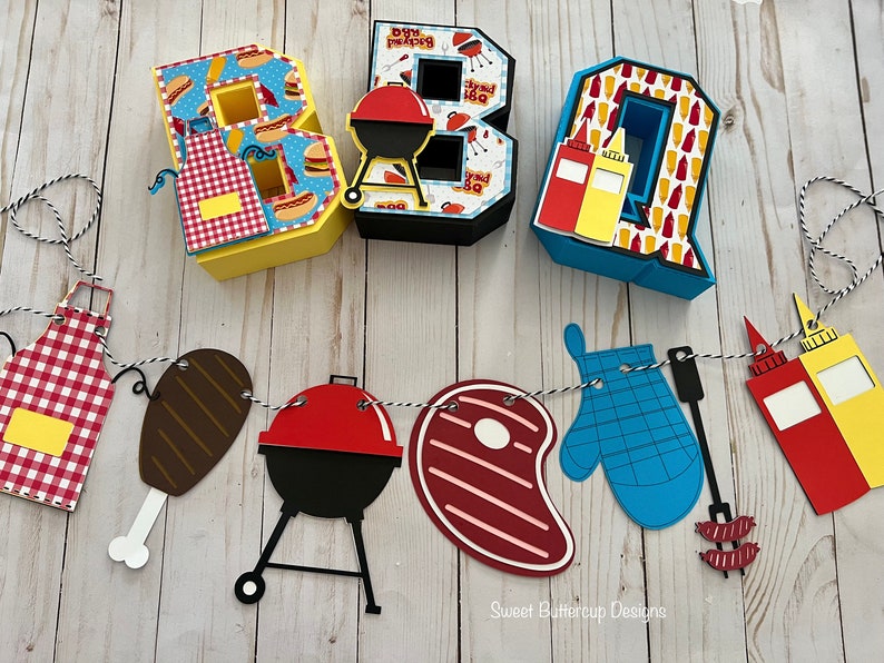 May include: Three-dimensional letters spelling BBQ, decorated with food patterns, alongside a hanging banner featuring cutouts of a red and white checkered apron, a chicken leg, a charcoal grill, a steak, a blue oven mitt, and condiment bottles.