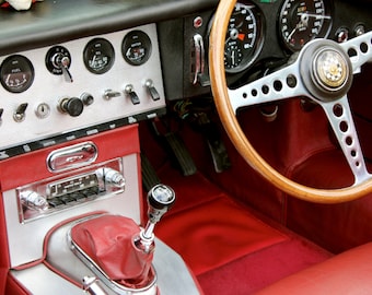 May include: The interior of a classic car with a wooden steering wheel, red leather seats, and a dashboard with gauges and controls.