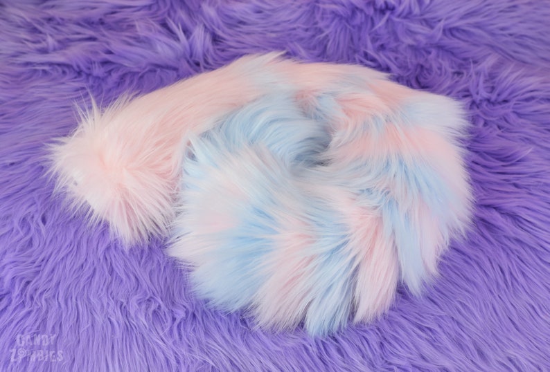 May include: A close-up of a soft, fluffy fabric in shades of pink and blue. The fabric is arranged in a swirling pattern, creating a visually appealing texture.
