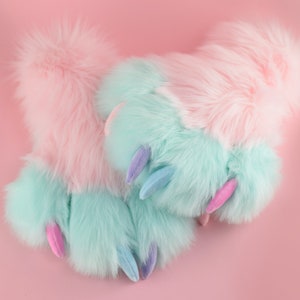 May include: A pair of fuzzy pink and blue slippers with claw-like toes. The slippers are made of soft, plush fabric and have a whimsical design.