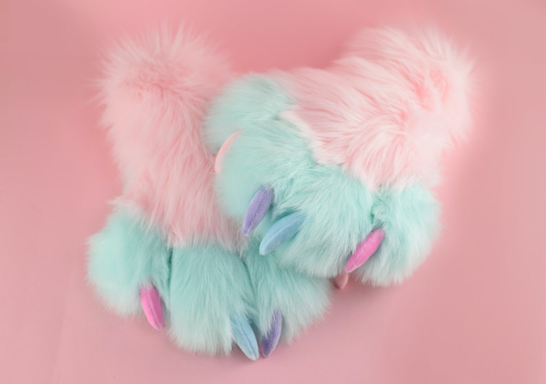 May include: A pair of fuzzy pink and blue slippers with claw-like toes. The slippers are made of soft, plush fabric and have a whimsical design.