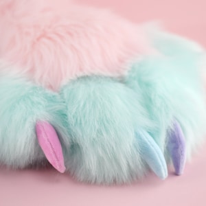 May include: A soft, plush paw with light blue and pink fur and claws. The paw is on a pink background.