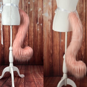 May include: A pink fluffy tail with a white ribbon attached to the base. The tail is on a white mannequin with a wooden base.