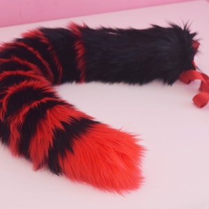 May include: A red and black striped faux fur tail with a black fur tip. The tail is attached to a red ribbon.