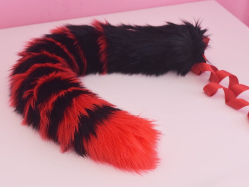 May include: A red and black striped faux fur tail with a black fur tip. The tail is attached to a red ribbon.