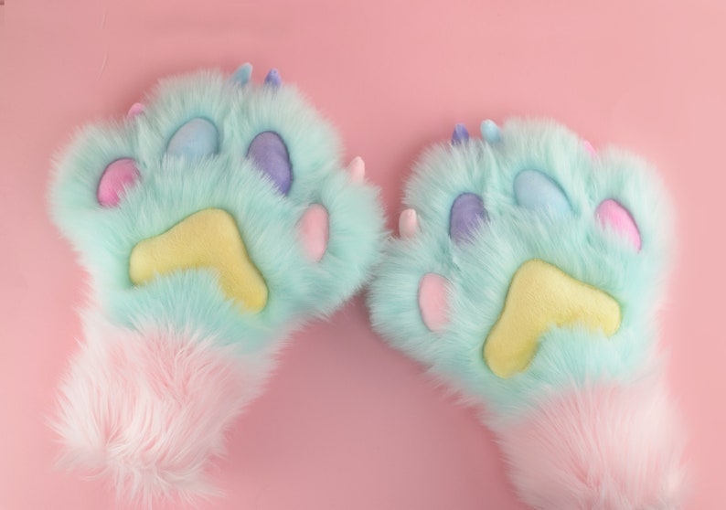 May include: A pair of light blue fuzzy paw-shaped hand warmers with pink and yellow accents. The hand warmers have a fluffy white cuff.