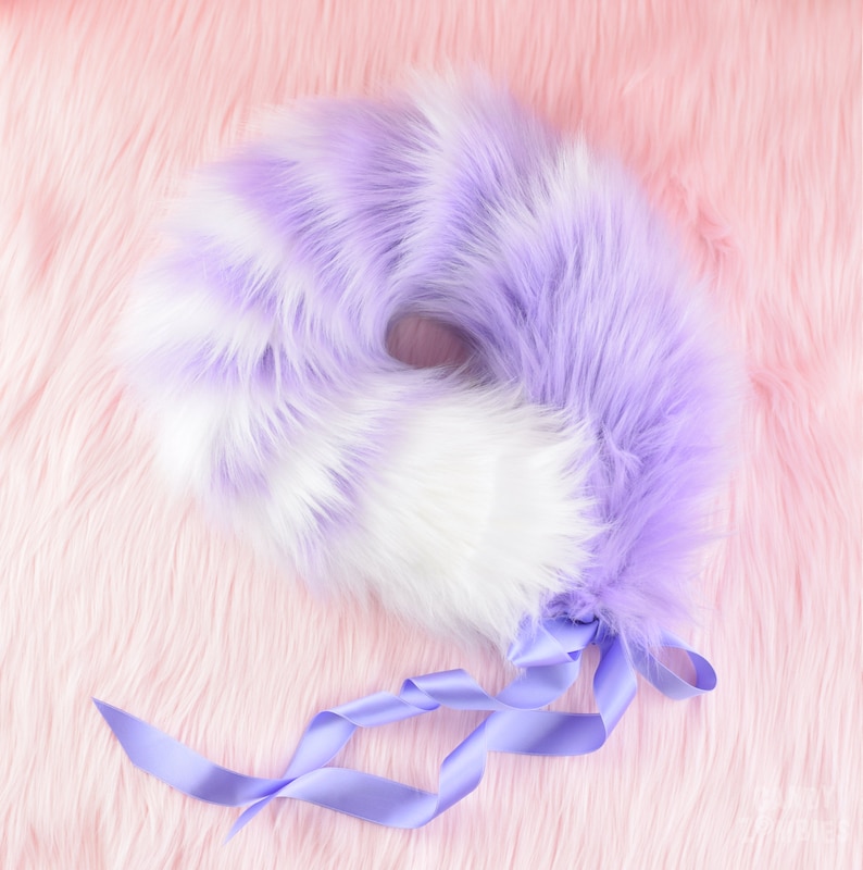 May include: A fluffy purple and white tail with a lavender ribbon. The tail is made of faux fur and is designed to be worn as a costume accessory.