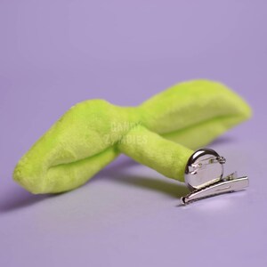 May include: A lime green plush sprout with a silver alligator clip. The sprout is shaped like a leaf with a rounded tip.
