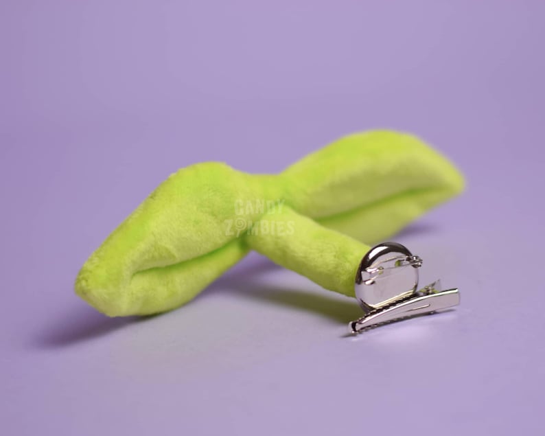 May include: A lime green plush sprout with a silver alligator clip. The sprout is shaped like a leaf with a rounded tip.