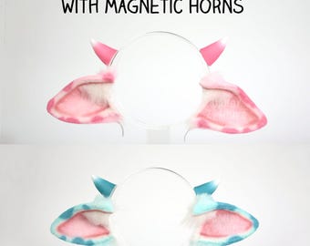 May include: Two headbands featuring faux fur cow ears with magnetic horns. The top set has pink and white spotted ears with pink horns. The bottom set has blue and white spotted ears with blue horns. Text reads: FAUX FUR COW EARS WITH MAGNETIC HORNS.