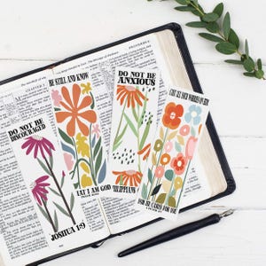 Puede incluir: Tres marcadores de flores coloridos con versículos bíblicos inspiradores. Los marcadores presentan una variedad de flores en tonos de rosa, naranja, amarillo y azul. Los versículos son "No te desanimes", "Estate quieto y sabe", "No te preocupes", "Echa todas tus preocupaciones sobre él", "Yo soy Dios", "Filipenses 4:6", "Porque él cuida de ti".
