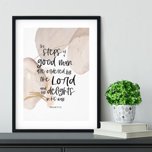 May include: A printable wall art print with a watercolour background in shades of pink and gold. The print features a quote from Psalm 37:23: "The steps of a good man are ordered by the Lord and He delights in his way."
