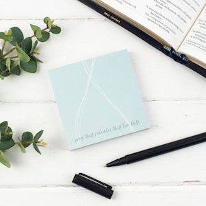 May include: A light blue sticky note with white lines and the text "pray this! remember this! live this!" on a white wooden surface.