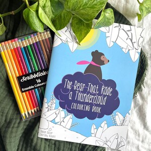 May include: A coloring book titled "The Bear That Rode a Thundercloud" with a black bear riding a cloud. The book is open to a page with a black and white illustration of the bear on the cloud. A set of 16 erasable colored pencils is next to the book.