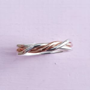 May include: A silver and rose gold intertwined ring. The ring is made of two separate bands that are twisted together.