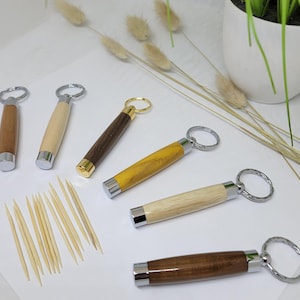 Peut inclure: Cinq cure-dents en bois avec des anneaux de clés argentés. Les cure-dents sont faits de différents types de bois, dont le brun clair, le brun foncé et le jaune. Un tas de cure-dents en bois se trouve dans le coin inférieur gauche de l'image.