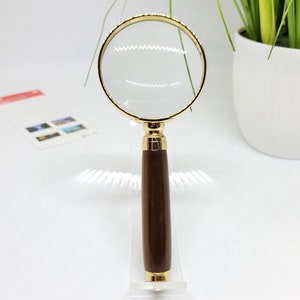 May include: A magnifying glass with a gold-colored frame and a brown wooden handle.