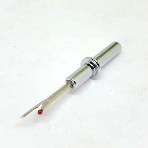 May include: A silver sewing thread cutter with a red tip. The cutter is retractable and has a metal casing.