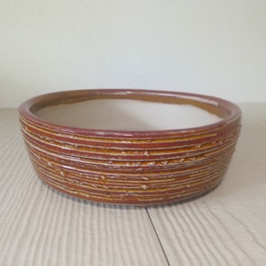Peut inclure: Un pot rond en céramique marron avec un intérieur émaillé blanc. Le pot a un design texturé à rayures.