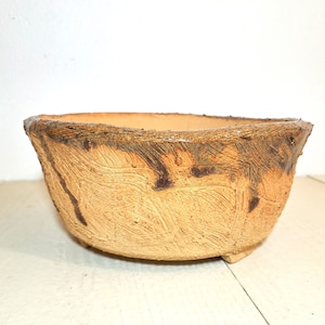 May include: A handcrafted, oval-shaped ceramic planter with a textured, light brown exterior. The rim features a darker brown, glazed finish. The planter has a rustic, artisanal appearance, suitable for indoor or outdoor use. The planter is approximately 12 inches wide.