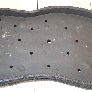 Op de afbeelding: Een donkergrijze, onregelmatig gevormde keramische plantenbak met een getextureerde rand en talrijke drainagegaten. De plantenbak is ontworpen voor planten en meet ongeveer 46 cm lang en 25 cm breed.