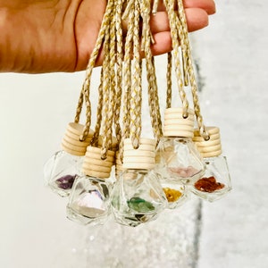 May include: A collection of small, clear glass bottles filled with colorful gemstones. Each bottle has a wooden cap and is suspended by a braided, gold-flecked cord. The bottles are held together, showcasing the variety of crystals.