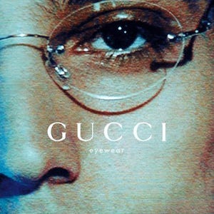 Może przedstawiać: Zbliżenie oka w okularach Gucci bez oprawek. Reklama zawiera logo Gucci i słowo "eyewear" jasną czcionką. Obraz ma wygląd vintage, lekko spikselizowany.