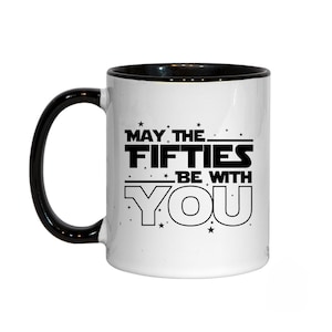 May include: White ceramic mug with a black rim and handle. The mug features a black graphic that says "May the Fifties Be With You" with stars around the text.