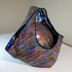 May include: A fabric tote bag featuring a vibrant pattern of diagonal multicoloured stripes in pink, yellow, blue, and black. The interior lining displays a blue and white bowling pin print, and the bag contains a round, swirled bowling ball.