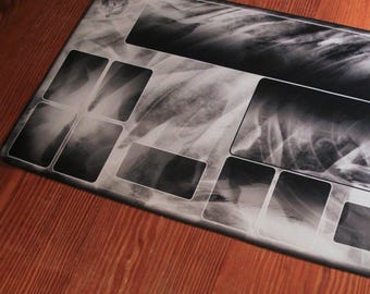 May include: A black and white gaming mouse mat with a textured, abstract design. The mouse mat has a rectangular shape and features multiple rectangular sections with a faded, cloudy pattern.