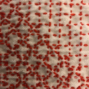 May include: White fabric with a red embroidered pattern. The pattern is a repeating geometric design of small squares and diamonds.