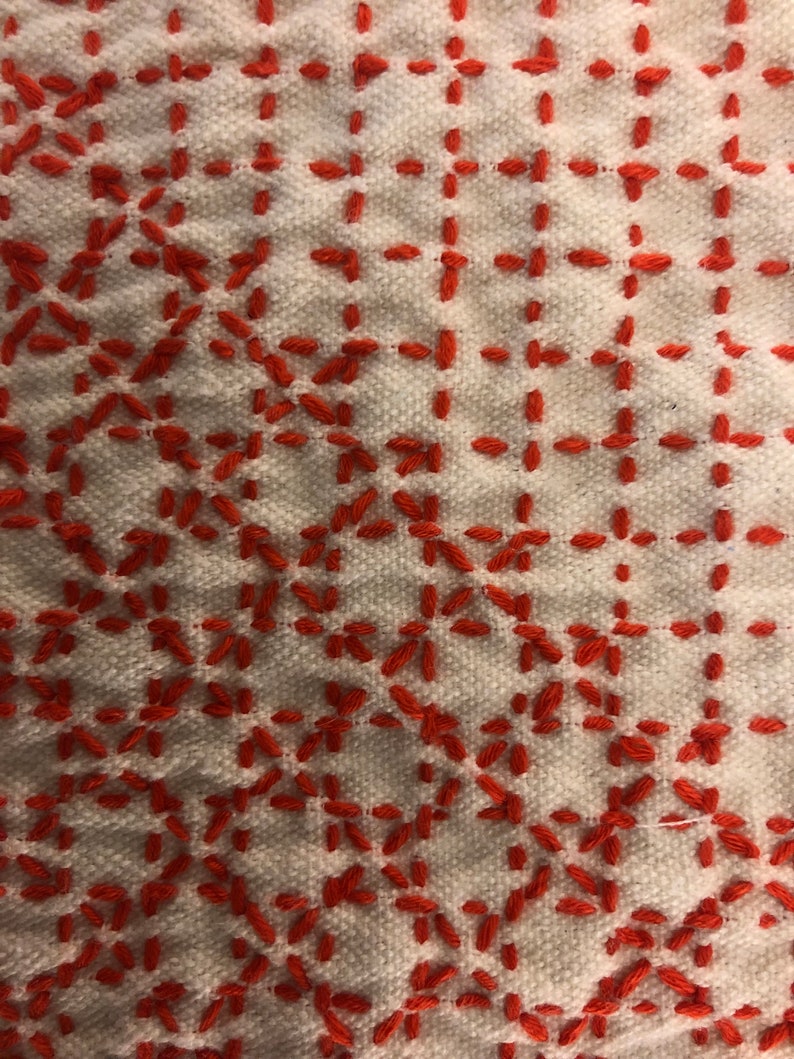 May include: White fabric with a red embroidered pattern. The pattern is a repeating geometric design of small squares and diamonds.