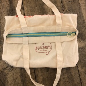 May include: A white canvas tote bag with a zipper closure and two handles. The bag has a red and white logo that says "Le Kivoltanti Fun Made".