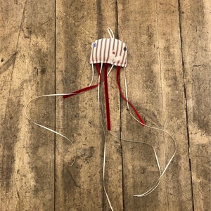 May include: A handmade striped fabric jellyfish toy with red and white ribbon tentacles hanging from a wooden surface.