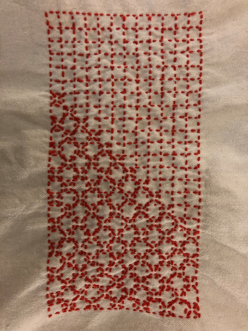 May include: A white fabric with a red embroidered design. The design is a grid pattern with a repeating floral motif.