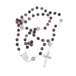 May include: A silver rosary with green and purple beads. The rosary features a silver crucifix and a silver medal with a religious image.